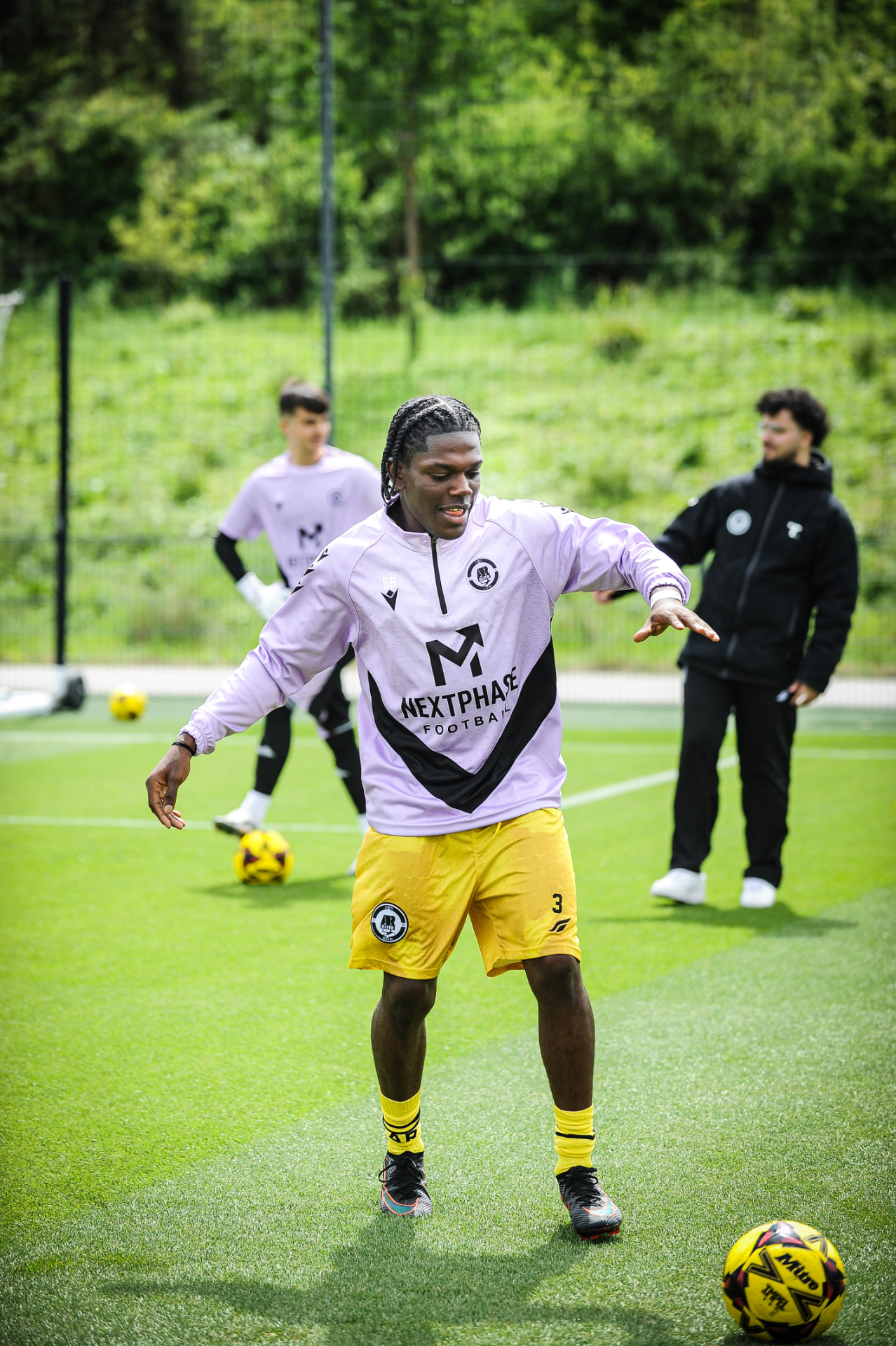A Next Phase Football player training on a sunlit grass pitch in branded kit.